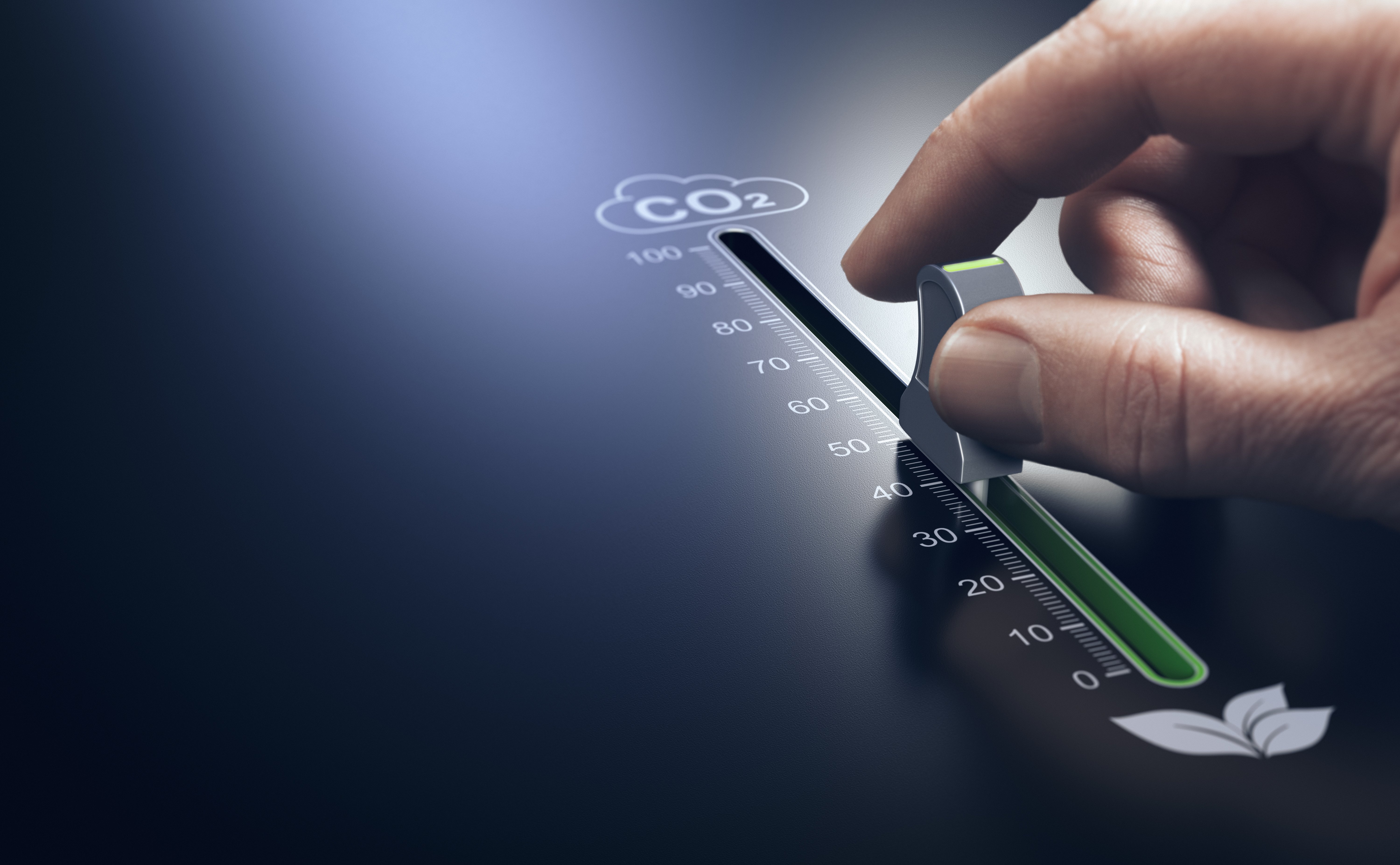 A hand moves a slider on a CO₂ scale from a high value towards zero, symbolizing the reduction of emissions.