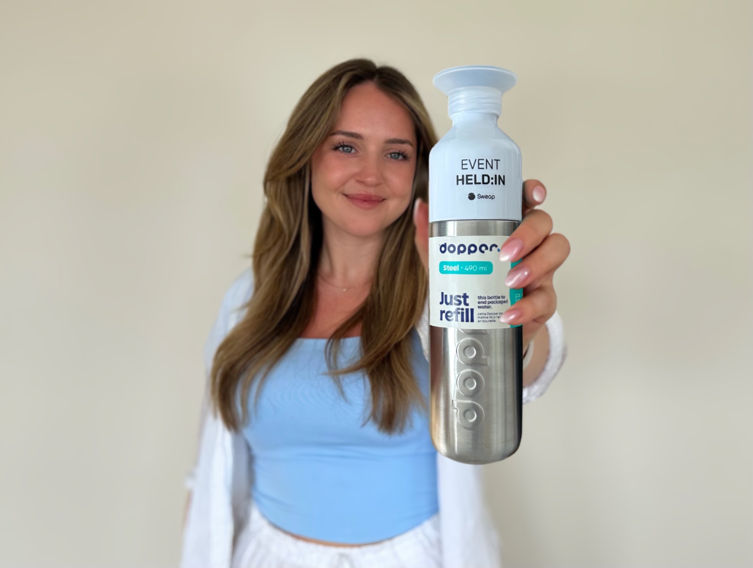 Mia from Sweap holds a reusable, Cradle to Cradle certified water bottle made of recycled steel with 'EVENT HERO' printed on it.