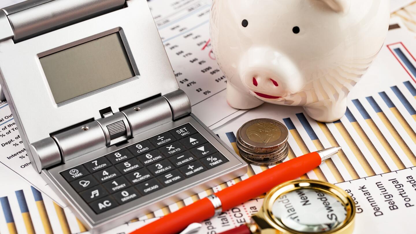 A calculator, piggy bank, coins, pen and magnifying glass sit on financial charts with country data a symbolic image for budget planning and cost analysis
