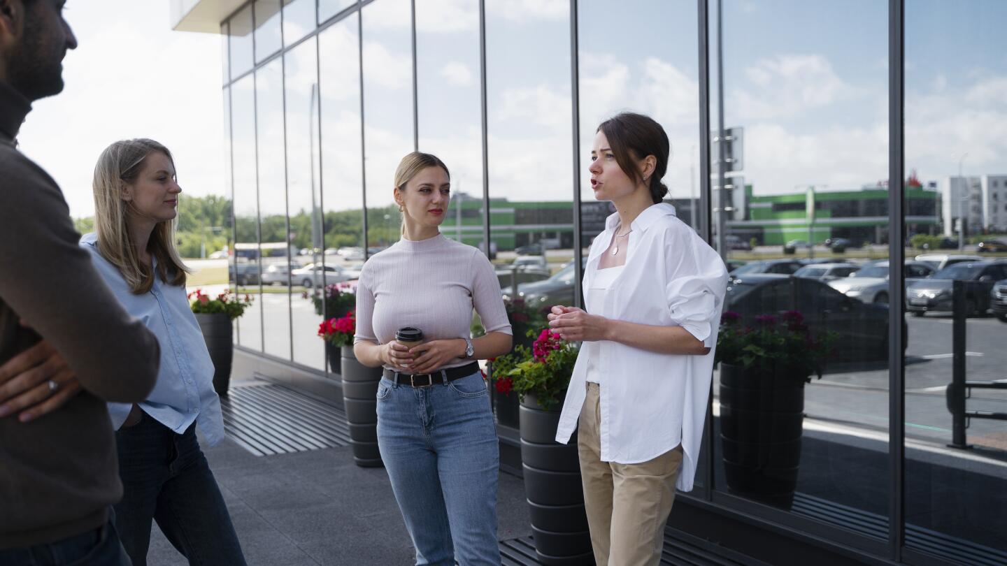 Drei Frauen unterhalten sich mit Kaffeebechern in der Hand vor einer verglasten Bürofassade