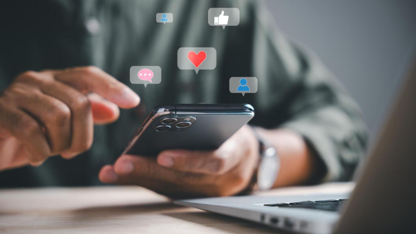 Hands holding a smartphone with floating social media icons like likes and hearts
