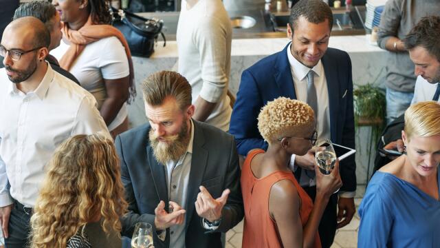 Blick von oben auf eine belebte Gruppe von Networking-Gästen, die in kleinen Grüppchen mit Getränken in der Hand angeregt diskutieren