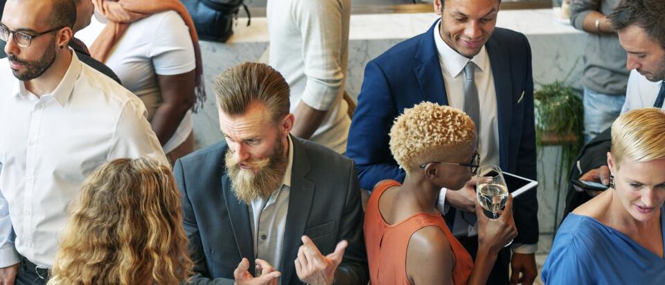 Blick von oben auf eine belebte Gruppe von Networking-Gästen, die in kleinen Grüppchen mit Getränken in der Hand angeregt diskutieren