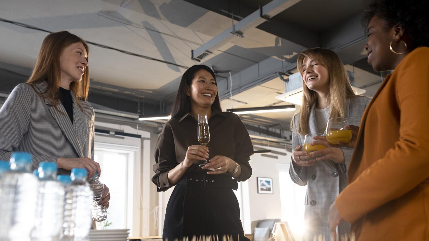 Four smiling women chat at a reception with drinks and finger food, water bottles and snacks in the foreground on the table