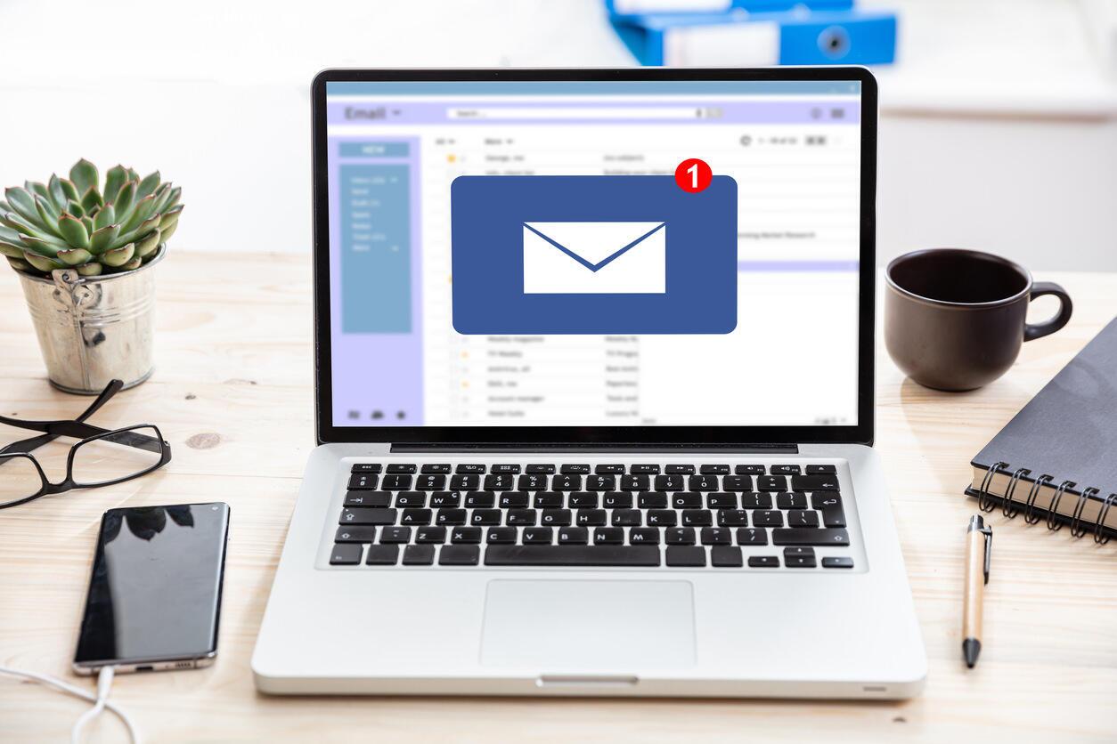 email message inbox on macbook on desk with phone, pen and coffee cup